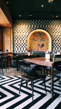 Chic cafe interior featuring wooden tables, stylish chairs, unique wallpaper, and geometric flooring design.