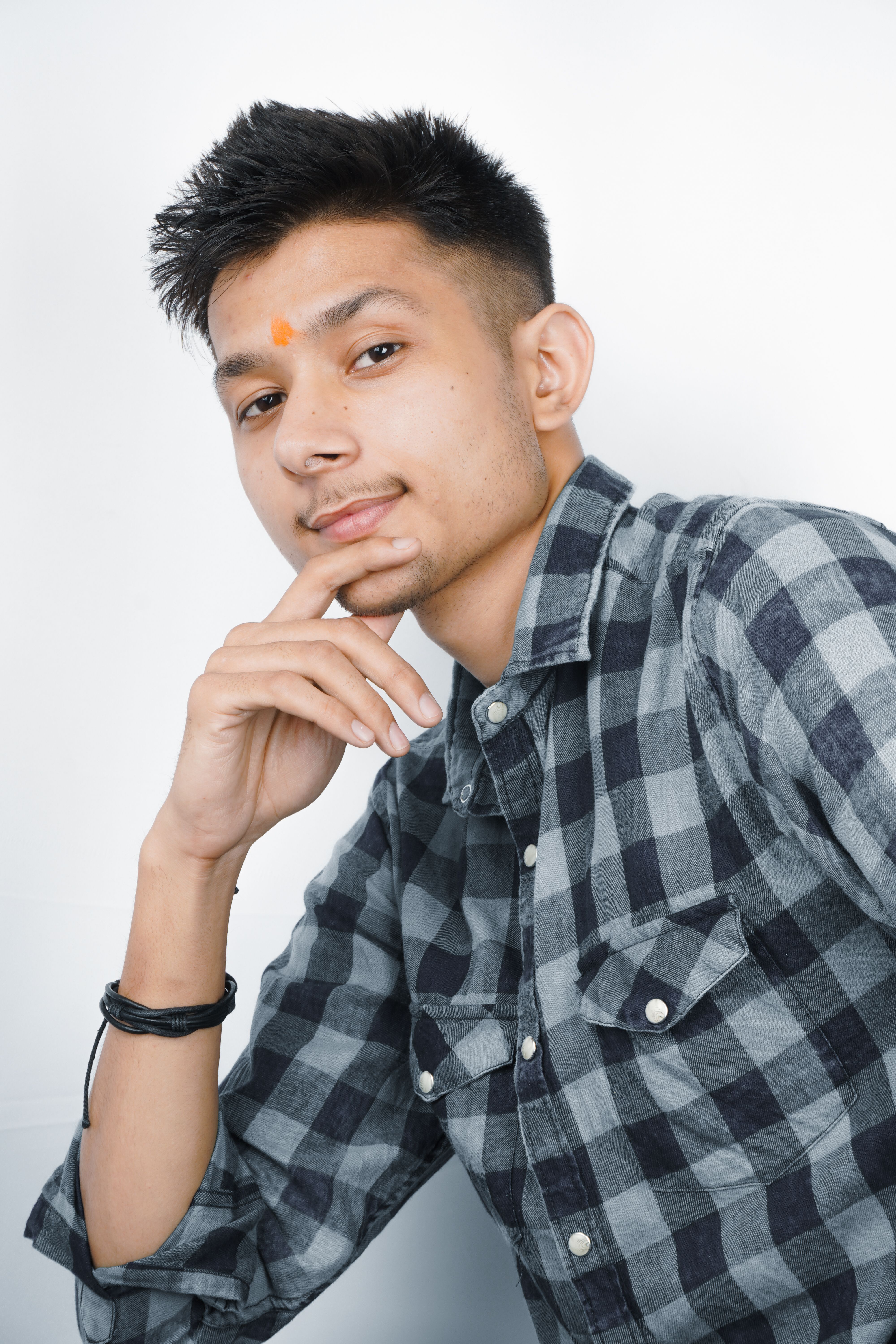 Portrait of a young man with hand on chin, wearing a checkered shirt, and looking thoughtful.