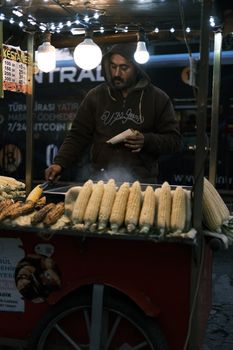 A street vendor in Istanbul selling freshly grilled corn from a food cart at night.