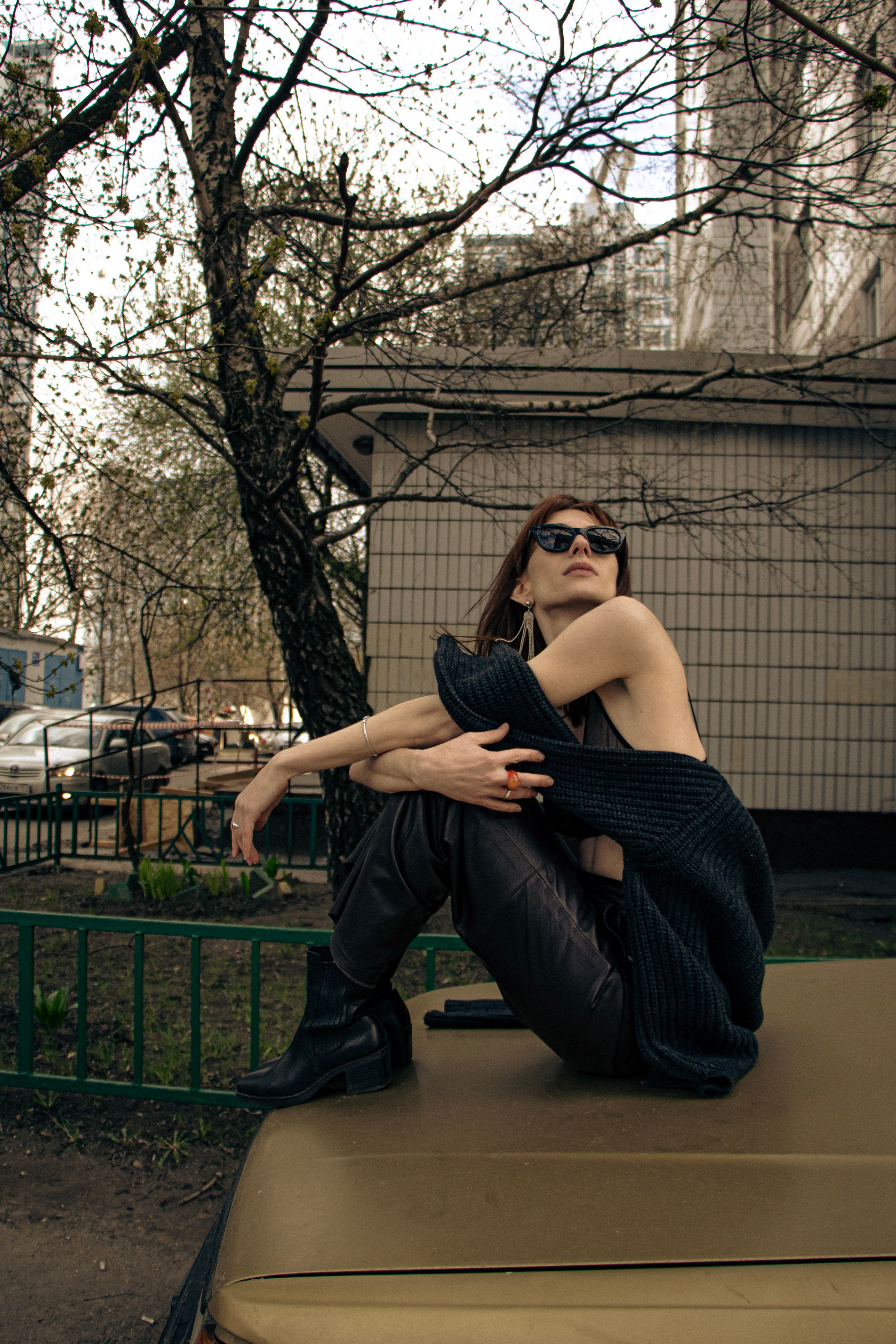 Fashionable woman posing with sunglasses on a car hood in urban outdoors.