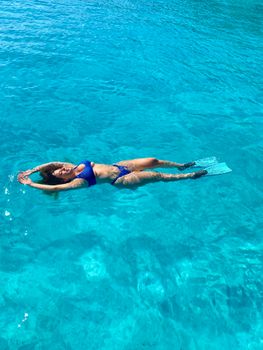 Woman floating in clear blue ocean in a bikini, enjoying a sunny vacation day.