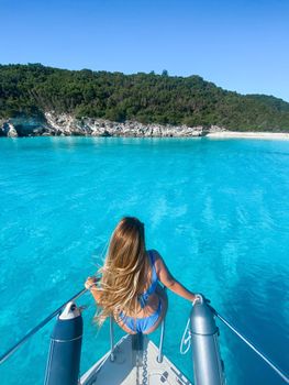 Woman in bikini enjoying a sunny day on a boat in clear blue waters near a rocky shore.