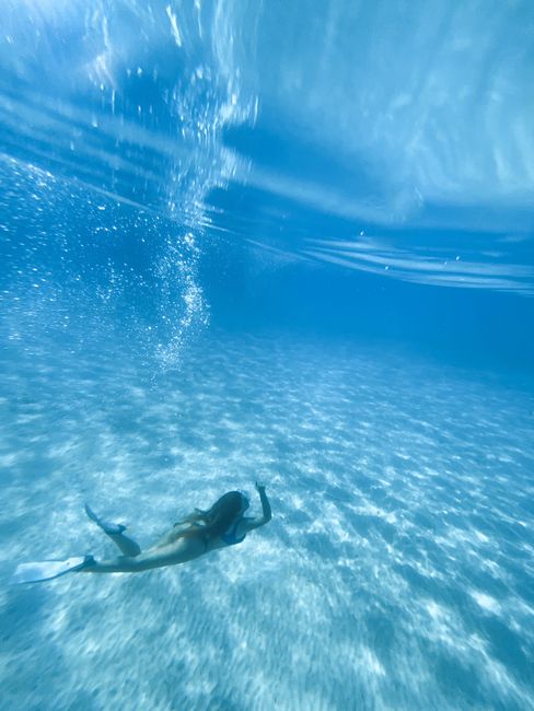 A woman gracefully swims underwater in a clear, azure ocean with sunlight filtering through.