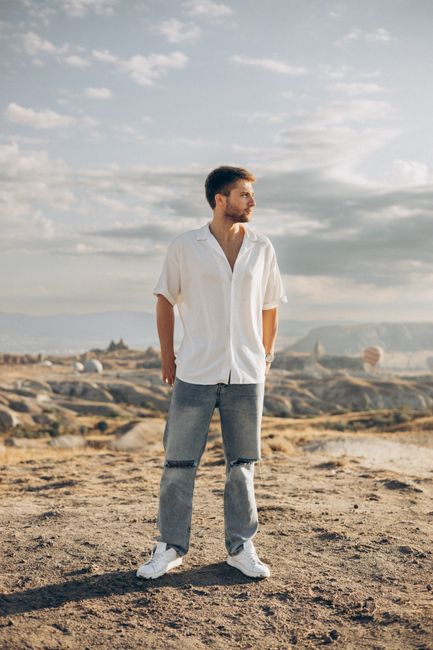 Young man in jeans and white shirt in Cappadocia, Turkey with hot air balloons in the background.