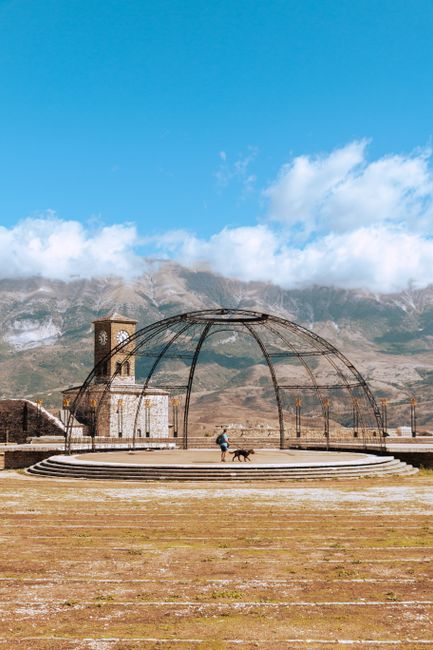 Person walking a dog by Gjirokaster Fortress with mountains in the background, capturing Albania's scenic beauty.
