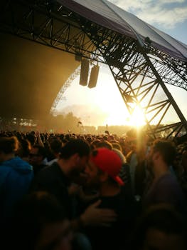 Energetic crowd at an outdoor music festival during sunset, featuring a large stage and vibrant atmosphere.