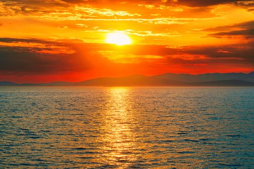 Free Vivid sunset over the ocean with dramatic orange sky and reflections. Stock Photo
