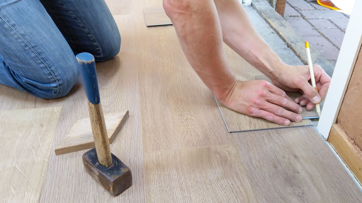 A flooring installer measuring and marking planks for a precise fit.