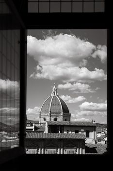 Black and white view of Florence Cathedral's dome framed by a window against a cloudy sky.