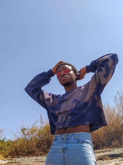 A fashionable adult male posing outdoors in casual attire under a clear sky.