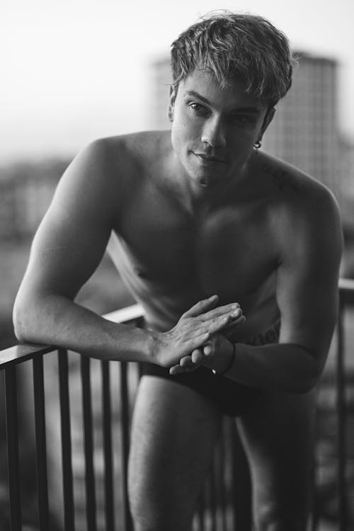 Grayscale Photo of Topless Man Leaning on Railing