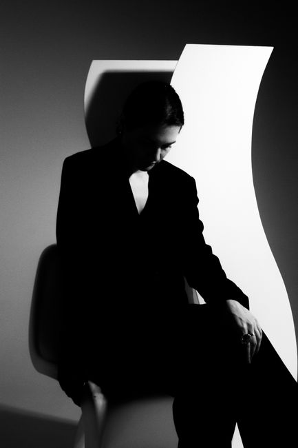 A woman in a suit sitting in a modern artistic setting, captured in black and white.