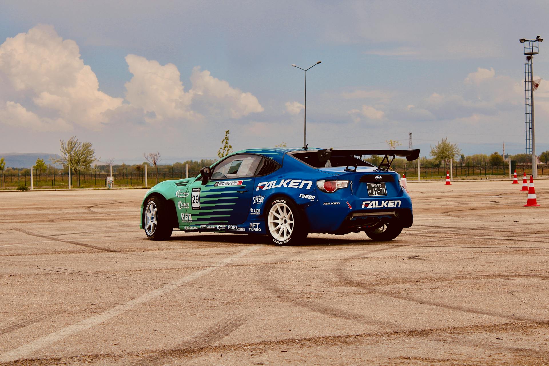 Blue sports car with sponsors showcased in drifting event on an outdoor track.