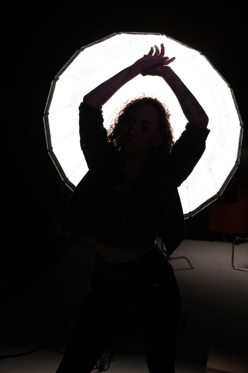 Free A dramatic silhouette of a woman posing with raised hands in front of studio lighting. Stock Photo