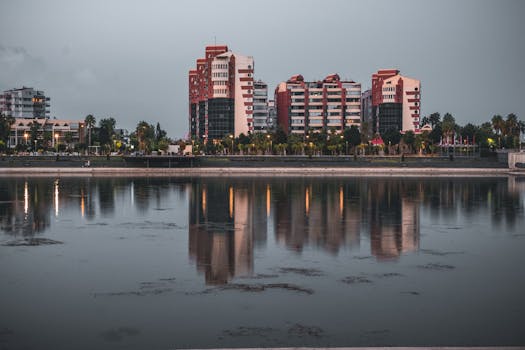 A beautiful cityscape featuring modern buildings reflecting on a tranquil waterfront at dusk, creating a serene urban landscape.