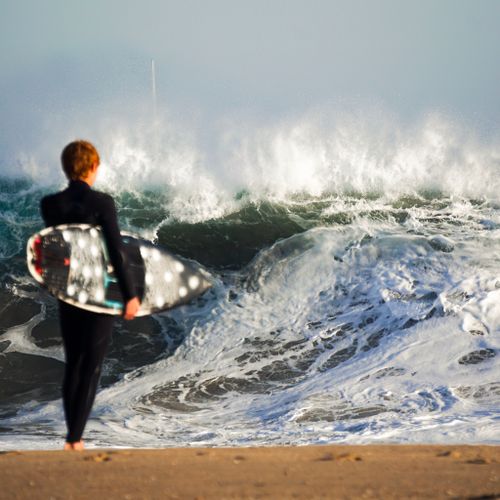 Free A surfer with a board stands on Newport Beach, CA, gazing at towering waves. Stock Photo