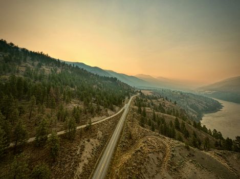 A stunning aerial shot of a winding highway through mountains and forests at sunset.