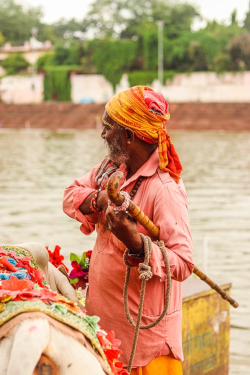 Free An elderly South Asian man stands beside a vibrant, decorated boat by the river. Stock Photo