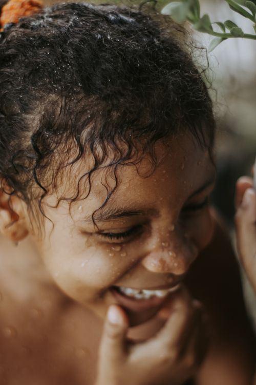 Free Close-up of a laughing child with water droplets and curly hair, radiating happiness. Stock Photo