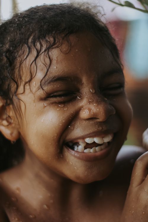 Free Close-up of a happy child smiling with water droplets on their face outdoors. Stock Photo