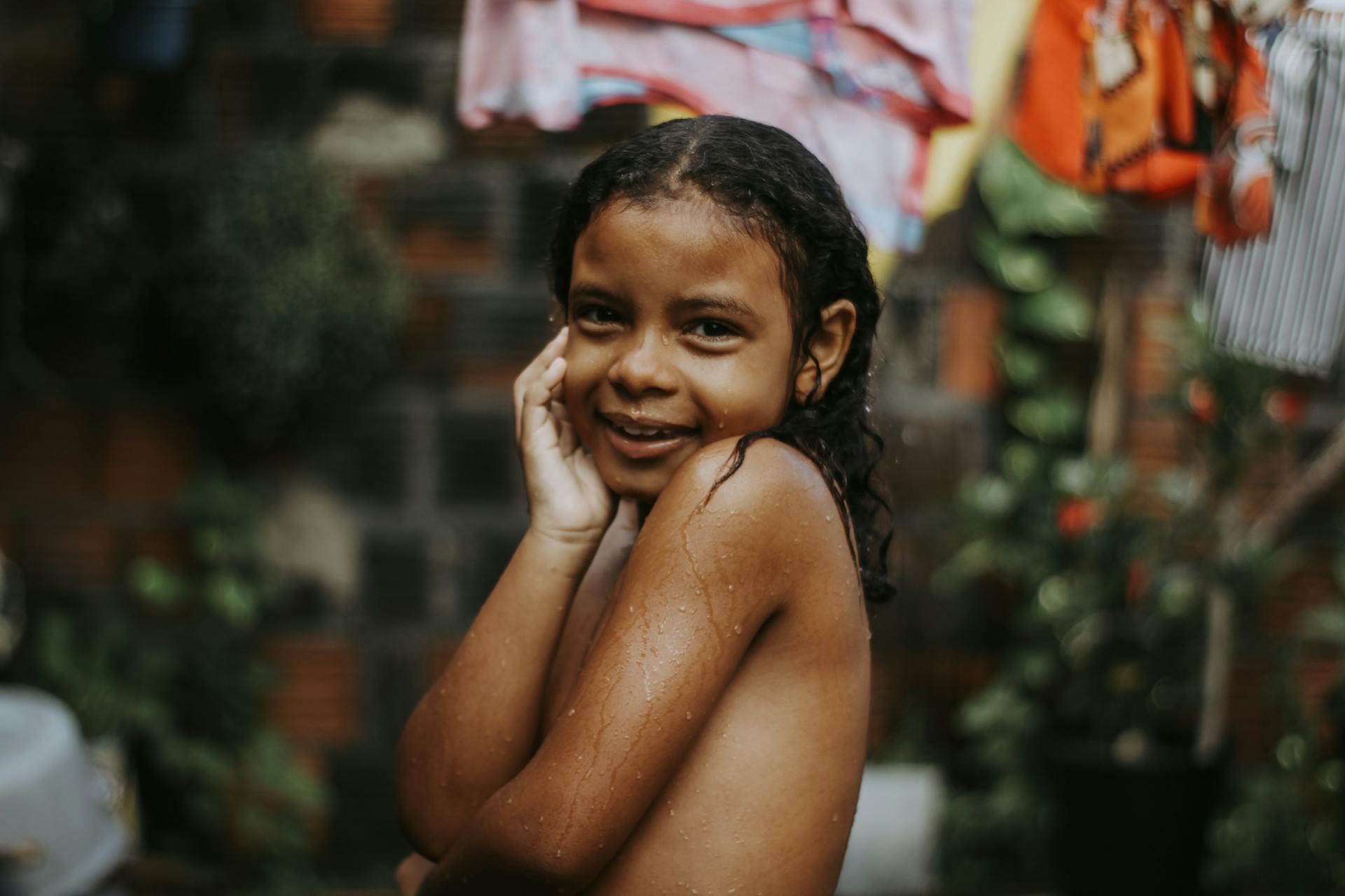 Smiling child with wet hair posing playfully outdoors after a refreshing rain shower.