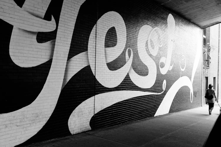 Person Walking Near A Brick Wall With Mural