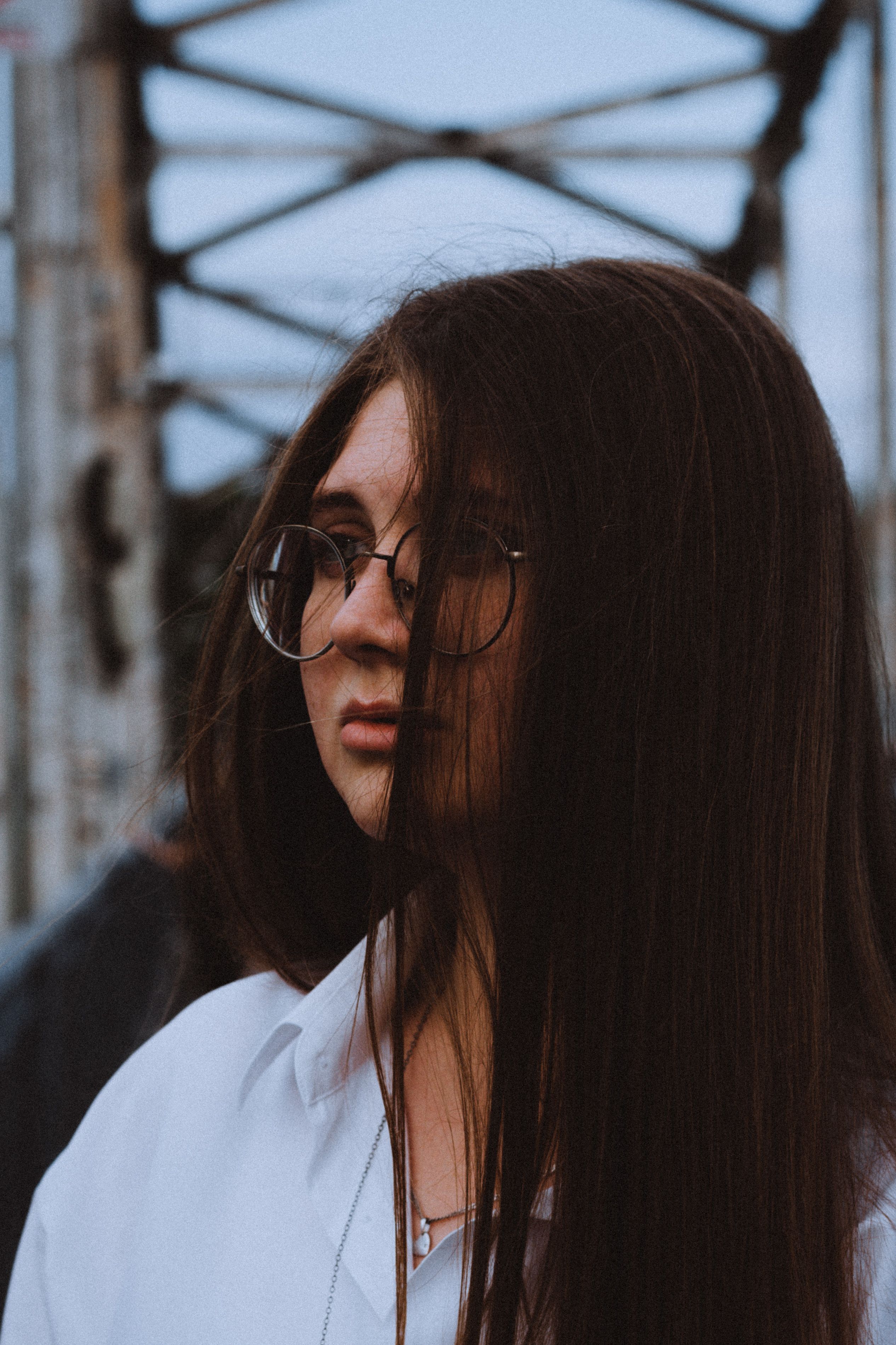 Portrait of a contemplative woman with long hair and eyeglasses standing on a bridge in Dnipro, Ukraine.