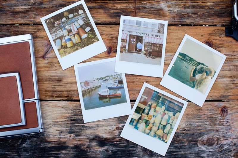 Instant photo prints and a leather album scattered on a rustic wooden table