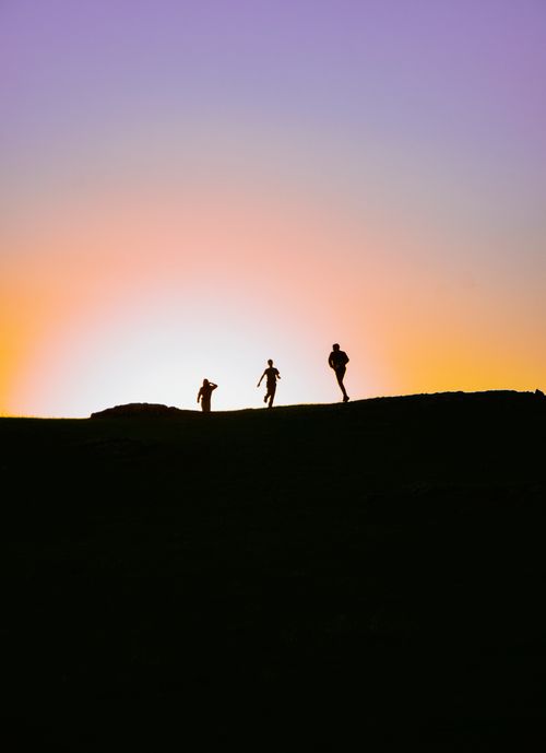 Free Silhouettes of people running on a hill during sunset, creating a vibrant sky backdrop. Stock Photo