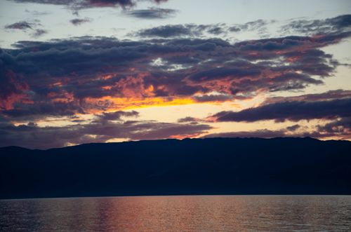 Free Silhouetted mountains and colorful clouds reflect on a tranquil lake at sunset. Stock Photo