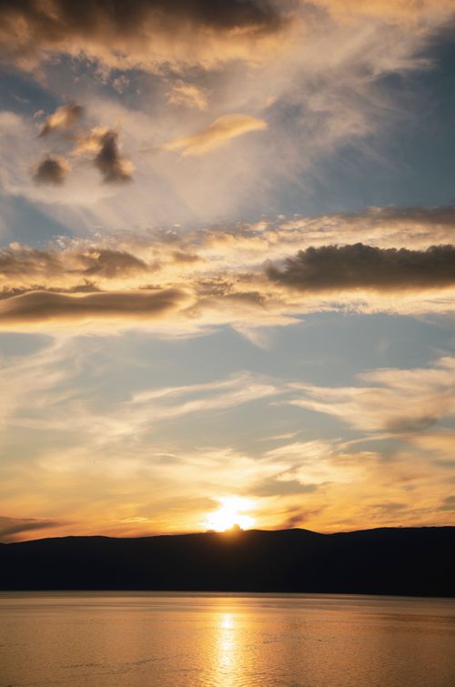 Free Tranquil ocean sunset with vibrant clouds and the warm glow of setting sun. Stock Photo