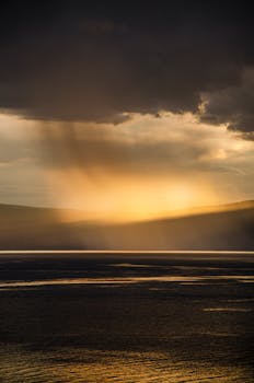 Golden sunlight breaking through dark clouds over a tranquil sea, creating a stunning scenic view.