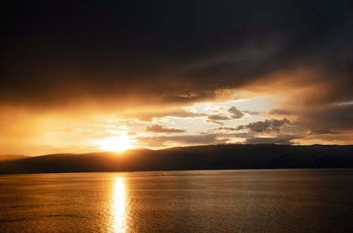 Free A View of the Ocean and a Silhouette of a Mountain in the Background during the Golden Hour Stock Photo