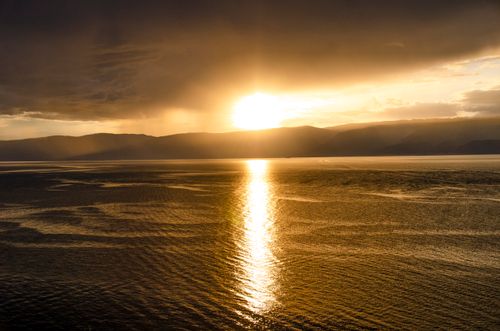 Free Golden sunset casting vibrant reflections over still waters and mountains, perfect for tranquility and nature themes. Stock Photo