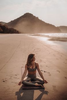 Woman in yoga pose on a tranquil beach with a scenic backdrop at sunset.