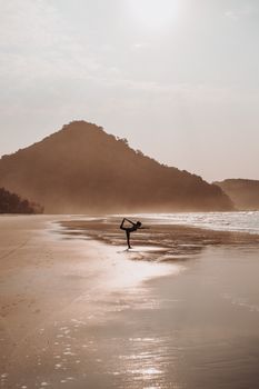 Silhouette of a woman practicing yoga on a tranquil beach during sunrise.