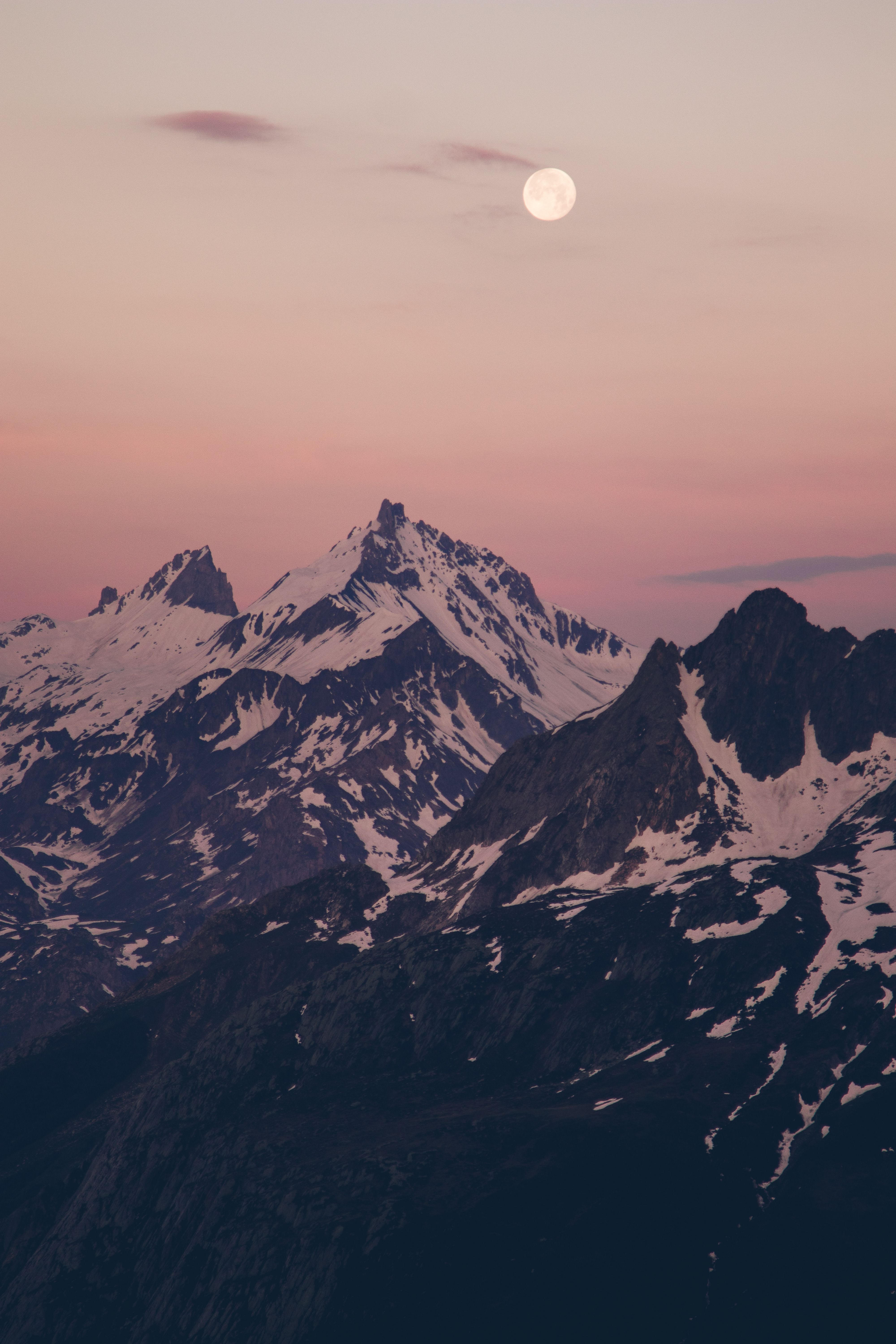 Captivating snowy mountain landscape at dusk with full moon and gentle hues of winter sunset.