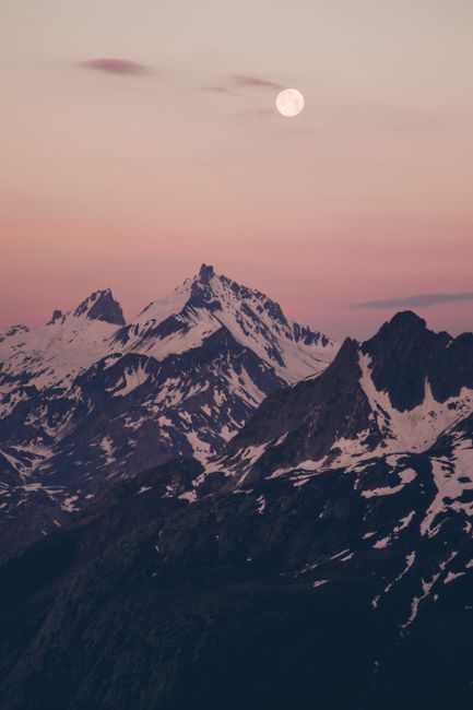 Captivating snowy mountain landscape at dusk with full moon and gentle hues of winter sunset.