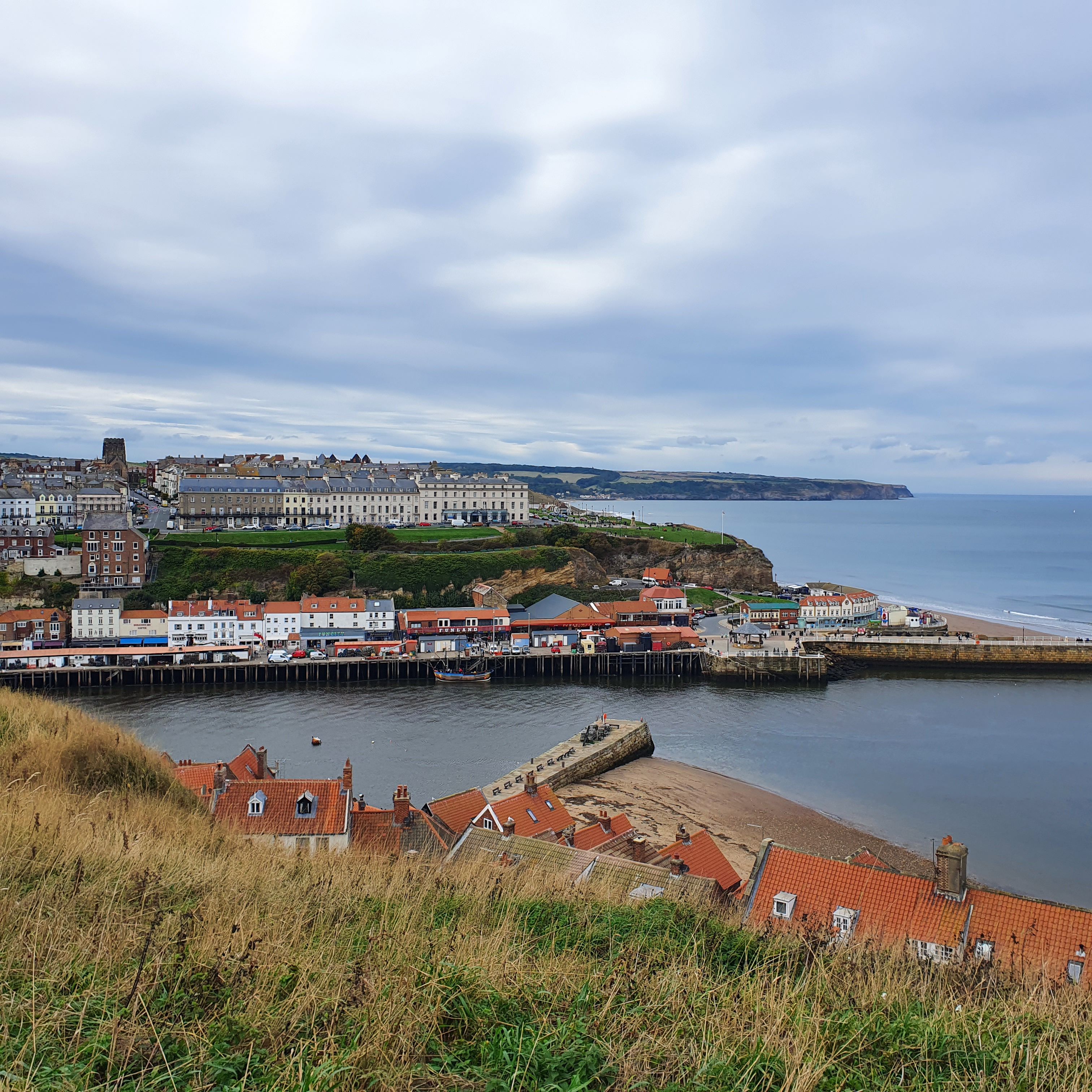 Whitby harbour and the coast towards Sandsend, red rooftops in the foreground under a wide sky.