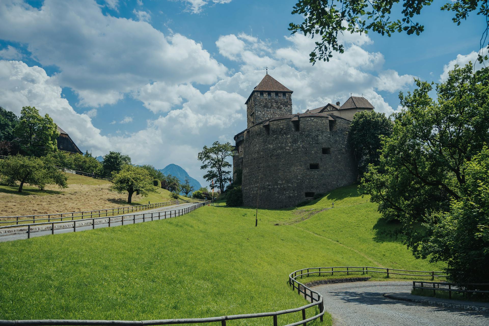 Charming landscape featuring Vaduz Castle, lush green fields, and a bright blue sky.