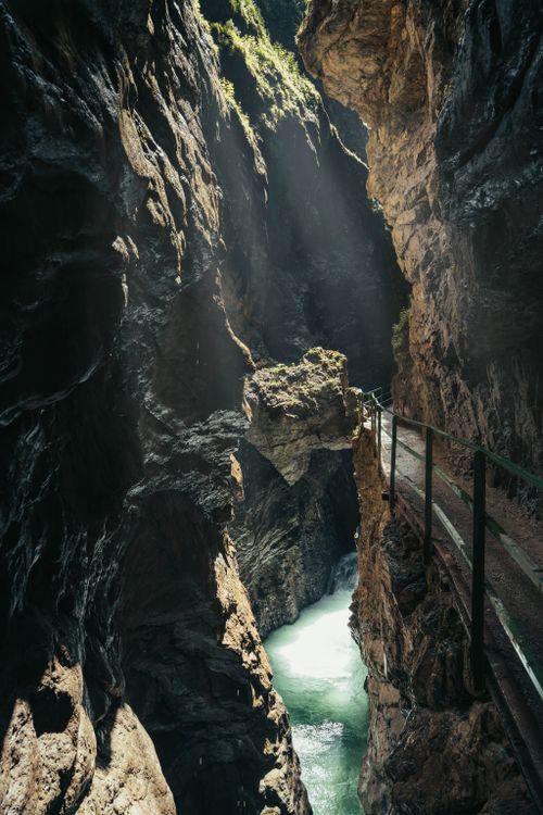Free Explore a breathtaking canyon with a footbridge and radiant sunlight illuminating the rugged rocks and vibrant river below. Stock Photo