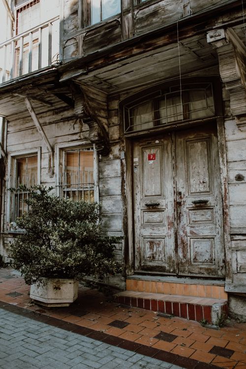 Free Weathered wooden doors on a rustic building facade with potted plant, conveying vintage urban charm. Stock Photo