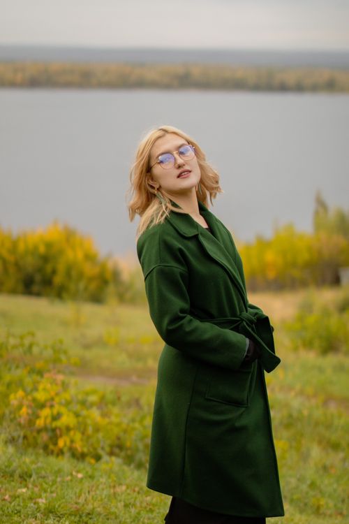Free Blonde woman in a green coat posing outdoors near a lake. Stock Photo