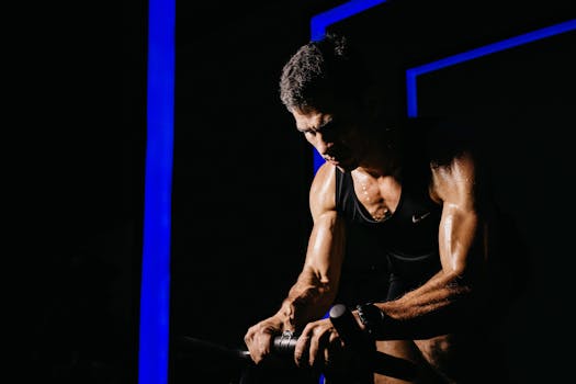 A brawny man in a black tank top intensely working out in a dimly lit gym.