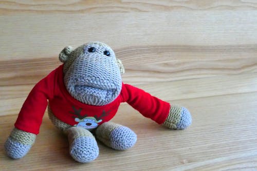 Poupée Amigurumi Singe Gris Portant Un Pull Rouge Sur Une Surface En Bois Marron