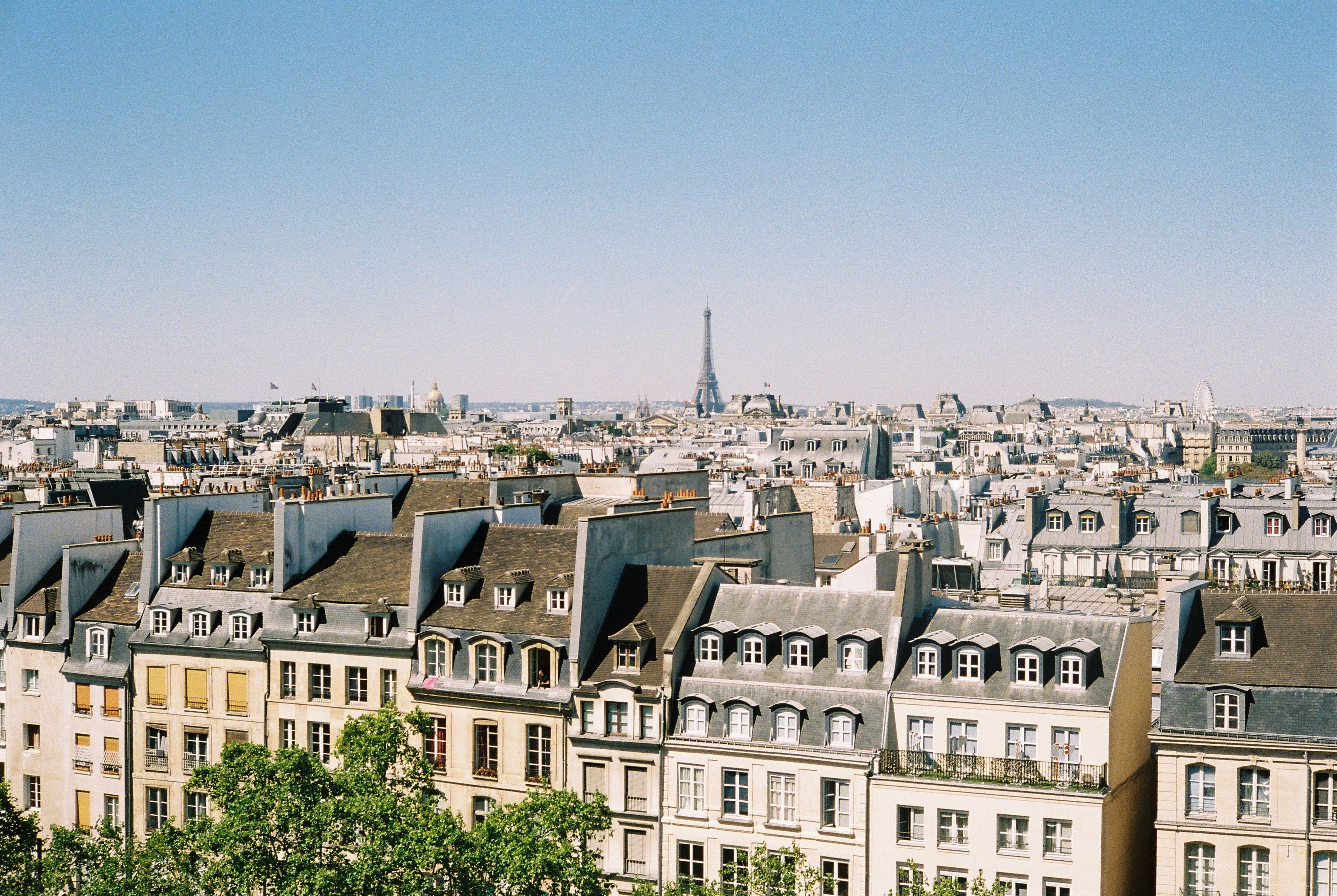 A scenic aerial view of Paris rooftops with the Eiffel Tower in the background under a clear blue sky.