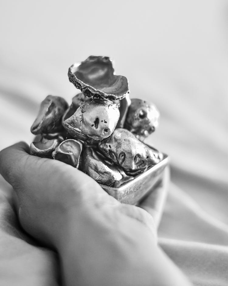 Black And White Photo Of Hand Holding Bowl With Metal Pieces