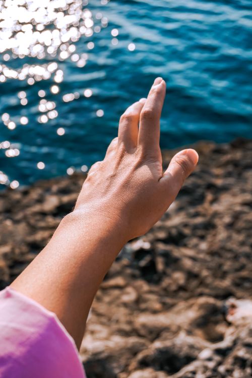 Free Close-up of a hand reaching towards the sparkling sea in Turkey, capturing the beauty of nature and human interaction. Stock Photo
