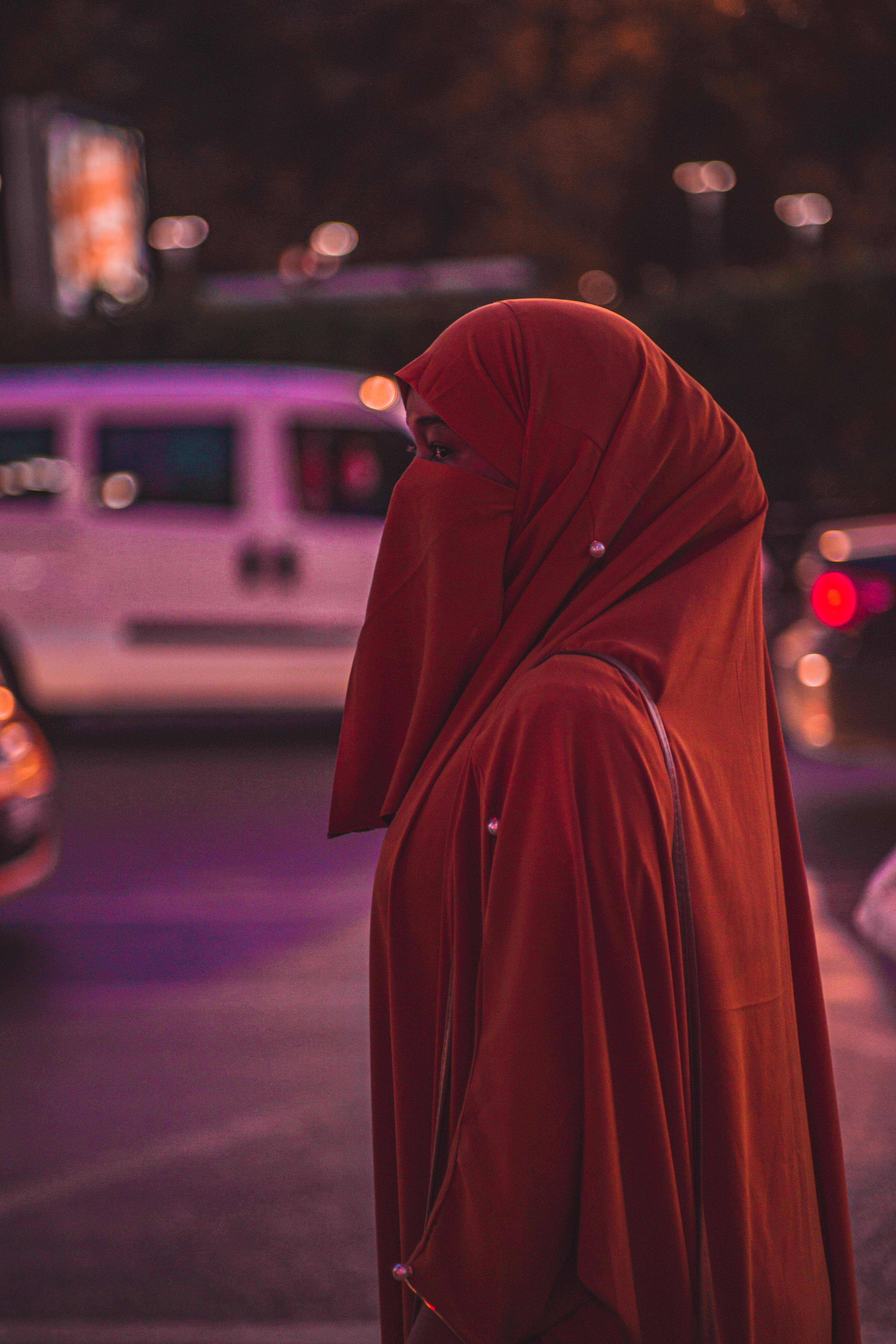 Woman in red hijab standing on a city street at night in a side view capturing traditional wear.