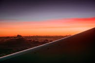 从飞机上俯瞰，云层之上日落景象生动，机翼清晰可见于前景